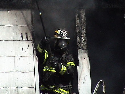 Volunteer fire fighter exiting live burn structure wearing NIOSH-certified SCBA, NFPA compliant turn-out gear, and holding a pike pole