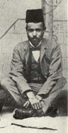 Photograph of a young man with a short beard, seated, wearing a Turkish fez.