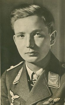 Hlava a ramena mladého muže, zobrazené v poloprofilu. Nosí vojenskou uniformu s železným křížem zobrazeným v přední části límce košile.
