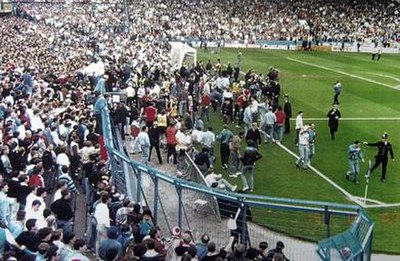 Liverpool supporters try desperately to climb the fence to reach the safety of the pitch while being stopped by the police.