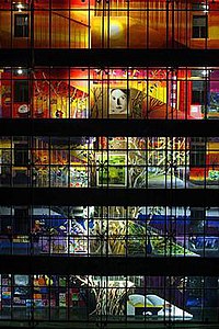 An illuminated, colorful mural painting distributed across the galleries and interior staircase along the five-floor facade of the interior courtyard of an office building