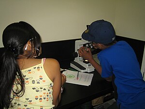 A Plant Investigator observes plant cells under a compound microscope Plant investigator in lab.JPG