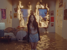 A still of Rodrigo standing in a room that she set on fire, from the music video for "Good 4 U". Good 4 U music video.png