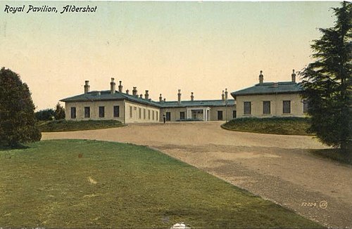 A postcard style image titled "Royal Pavilion, Aldershot". Picturing a white horseshoe shaped structure with a blue roof. In front of which is a gravel driveway, with a grassed area to the left side and trees either side.