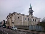 Side view of the church, entrance with columns and a spire covered by a green roof