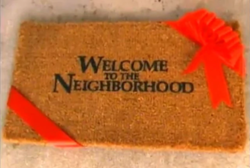 A title card for the American television series Welcome to the Neighborhood, featuring black letters on a brown doormat that has a red ribbon wrapped around two of its ends