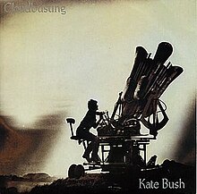 cover van de single van Kate Bush, waarop ze schrijlings op een reproductie van een 'cloudbuster' zit