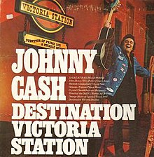Bir gitar tutan ve bir demiryolu vagonunun merdivenlerinde duran gülümseyen bir adam portresi.