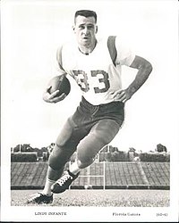 Fotografía en blanco y negro de Infante con uniforme de fútbol con protectores (pero sin casco), camiseta con el número 33 y sosteniendo una pelota de fútbol en el brazo derecho.