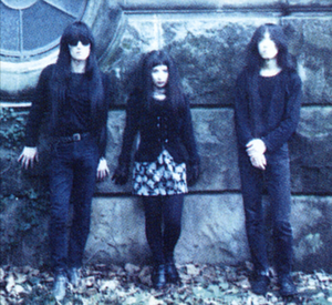 Two young men and a young woman stand in front of a wall.