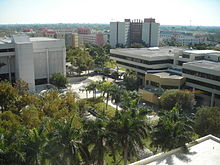 Modernist buildings on a green campus with palm trees, viewed from the roof or upper story of another building