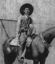A man wearing a wide brimmed hat on horseback