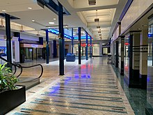 A color photograph of Gaviidae Common's lower level in 2021, displaying several empty storefronts, in addition to Walgreens, Planet Smoothie, Randstad, and Chameleon Shoppes.