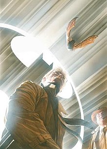 Comic book panel of Commissioner Gordon standing in front of the Bat-Signal, a bat flying at the top right of the panel in a photo-realistic style
