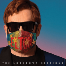 Elton John seen wearing sunglasses and a colorful face mask reading "ELTON" in red with stars on it.