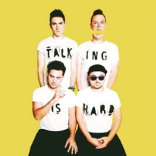 Участники группы Walk the Moon носят белые футболки с надписью Talking Is Hard на желтом фоне.