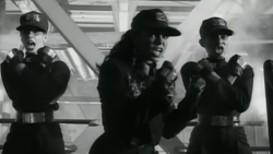 Jackson performing in the music video for Rhythm Nation, with dancers all outfitted in unisex black military-style uniforms.