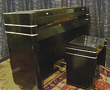 The minipiano 'Pianette' model viewed with its original matching stool: the wooden flap at the front of the instrument has been dropped revealing the tuning pins at the front.