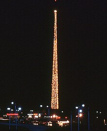 A nighttime photograph featuring a tall, thin tower festooned with lights