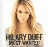 The portrait of a blonde woman sitting in front of a white background. She is sitting, looking into the camera. She is wearing a gray colored, full-sleeved top. To the bottom of the picture, the words "Hilary Duff" and "Most Wanted" are printed in grey block letters.