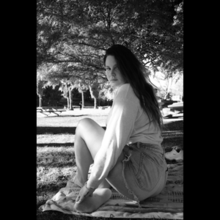 Cover art for "A&W": A greyscale photo of Lana Del Rey, who sits on a picnic blanket