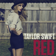 A photograph of Swift dressed in a white collared shirt, black shorts, and a brimmed hat standing with her back facing the camera. Her name Taylor Swift and the song's title Red are printed in capital letters at the bottom left of the photograph.