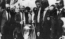 Trapattoni tiene tra le mani la prima Coppa dei Campioni della storia juventina, al ritorno a Torino dopo la tragica finale dell'Heysel: nei volti del tecnico e dei giocatori, l'amarezza per la tragedia che ha anticipato la partita.