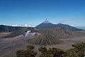 Vulcanul Bromo (craterul mare în stânga), in fundal se poate observa erupţia vulcanului Semeru.