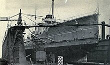 A large ship in a drydock, surrounded by construction equipment.