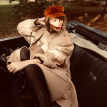 Swift wearing a red beret and beige trench coat, sitting in a convertible