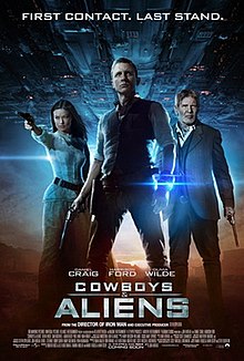 A man wearing a metal bracelet glowing a blue light on his left wrist, with a revolver in his right hand. To the left, a woman aiming a revolver. To the right, an older man wielding a revolver. In the background, a large metal object over a desert landscape. Above is shown "FIRST CONTACT. LAST STAND." Below them are the names of Daniel Craig, Harrison Ford, and Olivia Wilde above the title "COWBOYS & ALIENS", film credits, and theatrical release date.