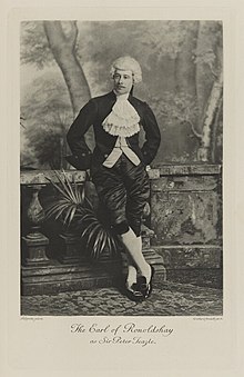 Black-and-white photograph of a man leaning against a balustrade richly dressed in an historical costume with a white wig