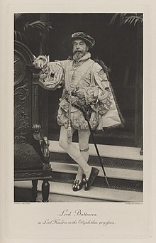 Black-and-white photograph of a standing man richly dressed in an historical costume with a sword and garter
