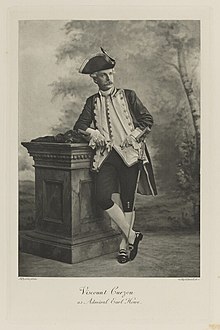 Black-and-white photograph of a standing man richly dressed in an historical costume with a tri-corner hat and sword