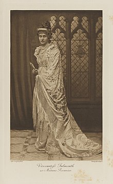 Black-and-white photograph of a standing woman richly dressed in an historical costume