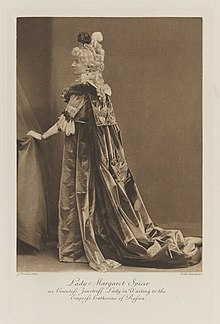 Black-and-white photograph of a standing woman richly dressed in an historical costume