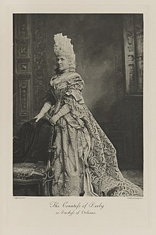 Black-and-white photograph of a standing woman richly dressed in an historical costume and a tall white wig