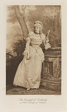 Black-and-white photograph of a standing woman richly dressed in an historical costume