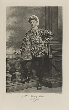 Black-and-white photograph of a standing man richly dressed in an historical costume with a sword