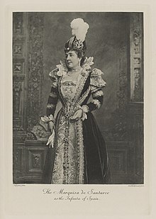 Black-and-white photograph of a standing woman richly dressed in an historical costume